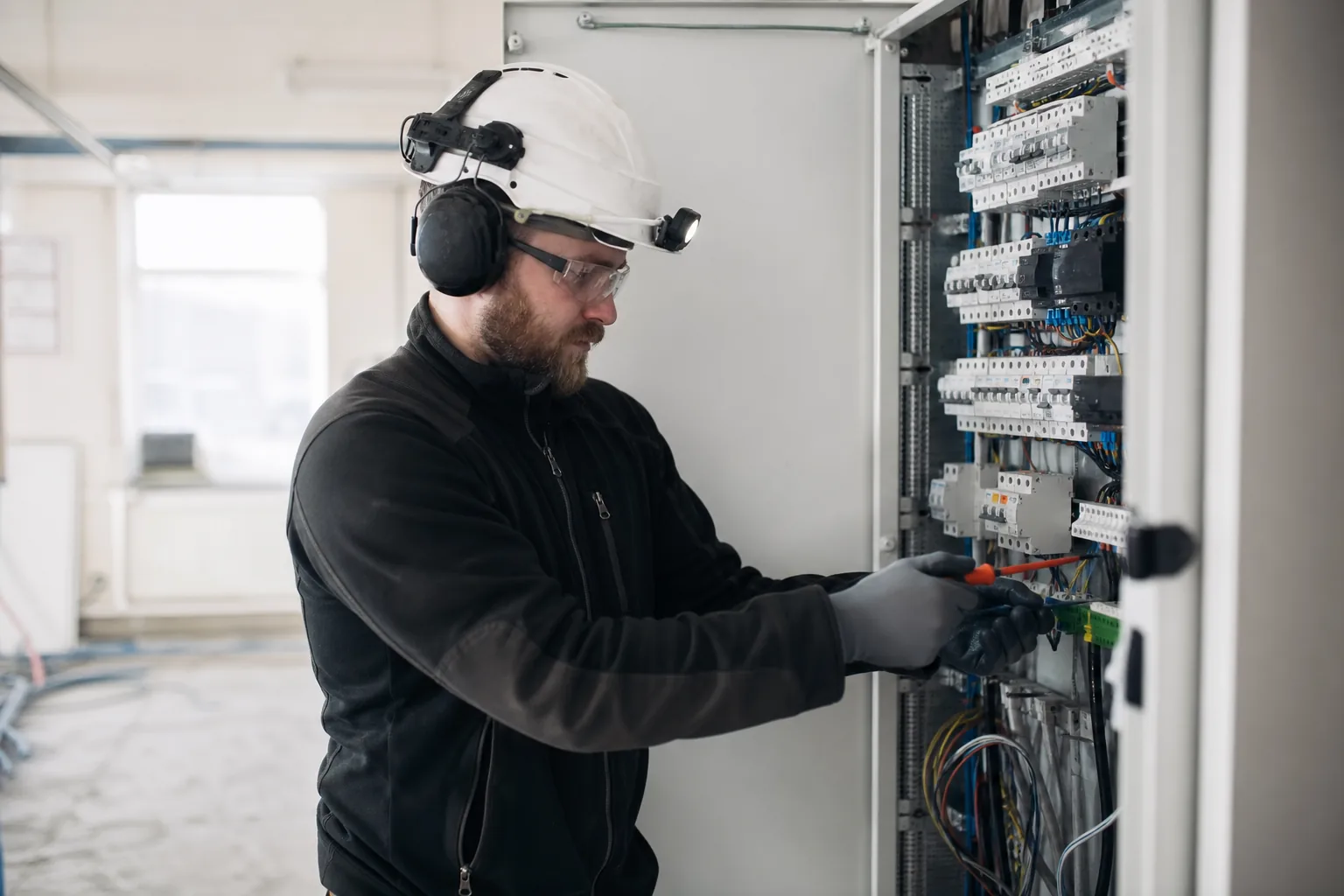 Elektriker med skyddsutrustning vid ett elskåp